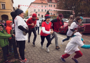 Dzieci z rodzicami biegną do mety chodnikiem przed przedszkolem