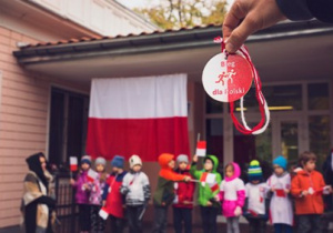 Dzieci stoją przed przedszkolem.Flaga biało-czerwona