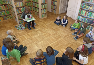 dzieci w bibliotece siedzą i słuchają czytanej książki