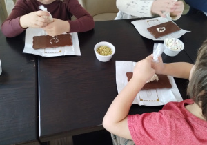 Dzieci ozdabiają czekoladę kolorowymi dodatkami.