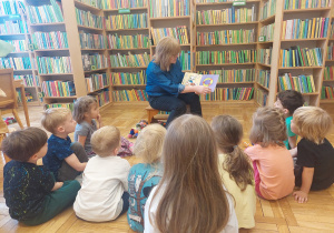Dzieci w bibliotece słuchają jak pani czyta książkę.