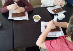 Dzieci ozdabiają czekoladę kolorowymi dodatkami.