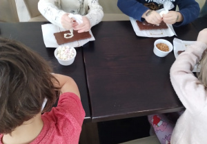 Dzieci ozdabiają czekoladę kolorowymi dodatkami.