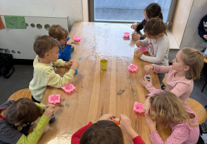 dzieci siedzą przy stole i mieszają w kubeczkach glicrynę