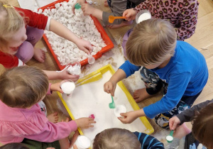 dzieci przesypują sztuczny śnieg łyżką do kubeczków