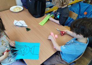 dzieci przy stoliku wycinają nożyczkami